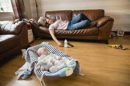 Exhausted mother having a nap on the sofa while her newborn child has a sleep.の写真素材