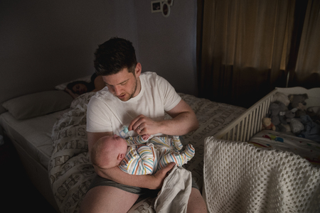 Father checking on his newborn baby boy at night as his wife stays asleep in bed.の写真素材