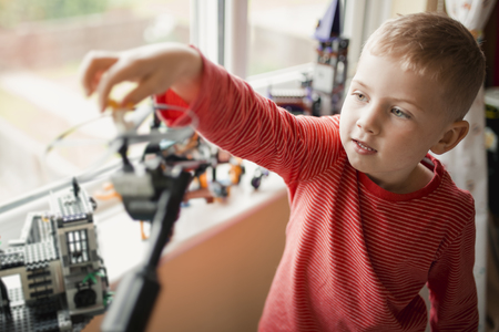 Little boy in a striped t-shirt playing with some toys in his room. She has streched his arm up to place and balace something while playing.の写真素材