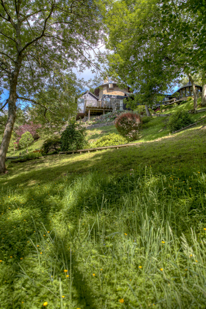 An uphill shot of a green meadow on a summers day, in the background is a modern house with a wooden patio.の写真素材