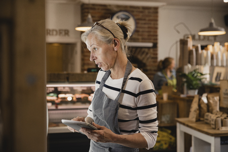 Mature coffee shop employee standing next to the fridges in the coffee shop performing a stock take.の写真素材