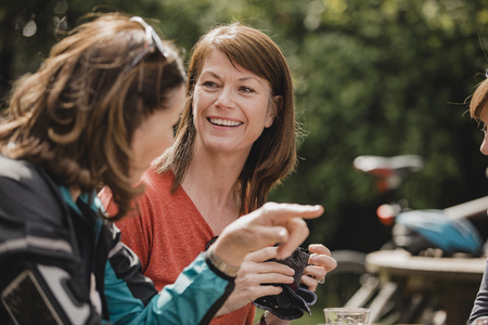 Small group of mature female cyclists sitting down in the outside seating area of a cafe. Tey are enjoying some refreshments as they take a break.の写真素材