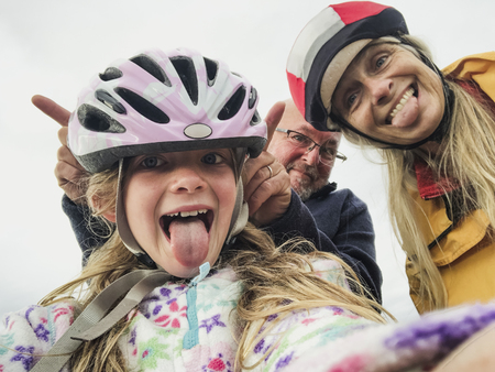 A close-up selfie of a happy family with one child, they are on an outdoor bikeride and pulling silly faces.の写真素材