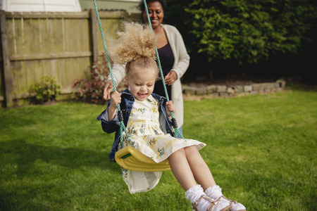 Little girl having fun while being pushed on a swing by her mother.の写真素材