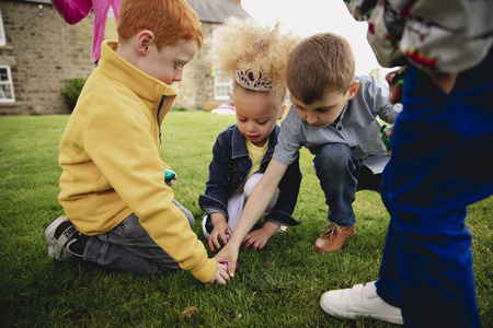 Group of young children kneeling down in a circle outdoors to share out the easter eggs that they have found.の写真素材
