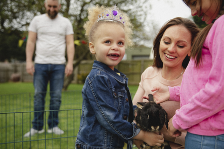 Little girl excited while stroking a pet rabbit ourdoors at a easter garden party.の写真素材