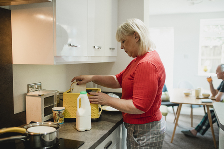 Mature woman is putting slices of white bread in a toaster at home for her breakfast.の写真素材