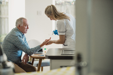 Senior diabetic man is having a check up at home from a district nurse. She is checking his blood glucose levels.の写真素材