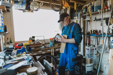 Senior man is working in his shed and is reading the label on a varnish.の写真素材