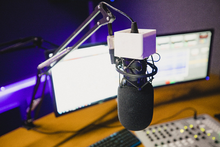 A front view shot of a radio station studio interior, a large desk is in the middle of the room, recording equipment and computers can be seen on the desk, a recording microphone is standing in position.の写真素材