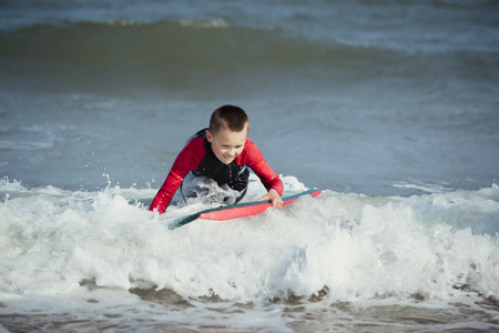 Little boy is trying to stand up on his surf board in the sea.の写真素材