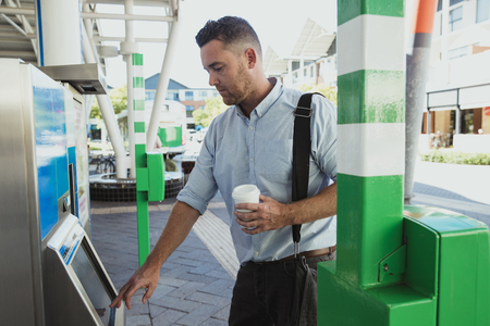 A side-view shot of a mid-adult businessman buying a train ticket to begin his commute to work, he...