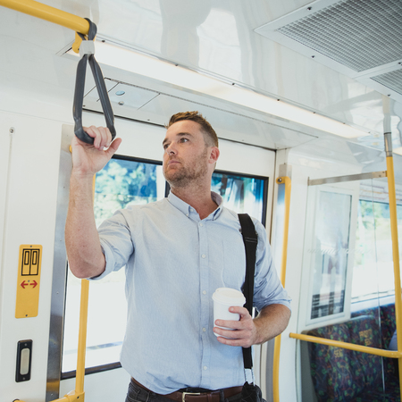 A side-view shot of a mid-adult businessman standing on a train commuting to work, he is holding a...