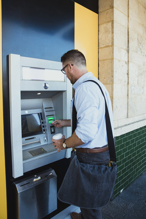 A rear-view shot of a caucasian businessman using an ATM machine in Perth Australia, he is inserting his credit card to withdraw money.の写真素材