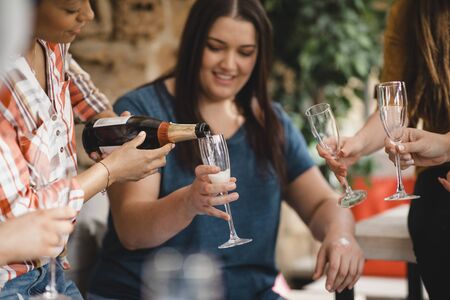 Small group of female friends celebrating with a glass of champagne. A woman is pouring the...