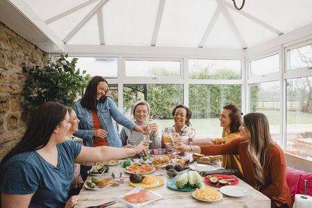 Small group of friends making a celebratory toast while sitting around a table in a conservatory.の写真素材