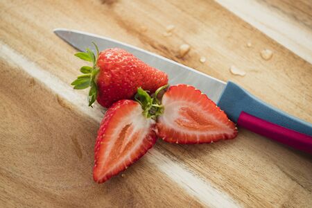 High angle view of strawberries, sliced, on a wooden chopping board next to a knife.の写真素材
