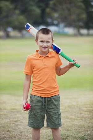 A portrait shot of a young caucasian boy wearing casual clothing, he is holding a cricket bat and...