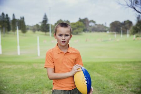 A portrait shot of a young caucasian boy wearing casual clothing, he is holding a rugby ball, he is looking at the camera.の写真素材