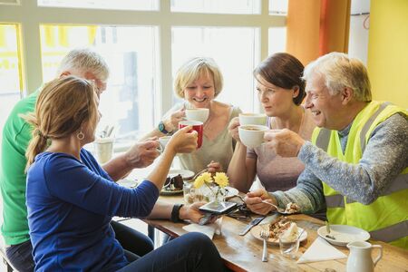 A group of five people taking a break from city cleaning and having coffee and cake.