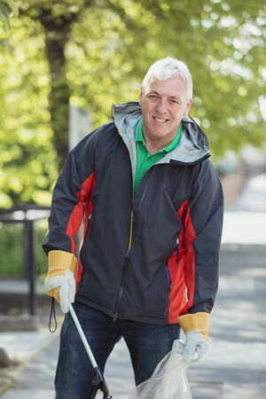 A portrait of a mature man standing in a park, participating in a city clean up.