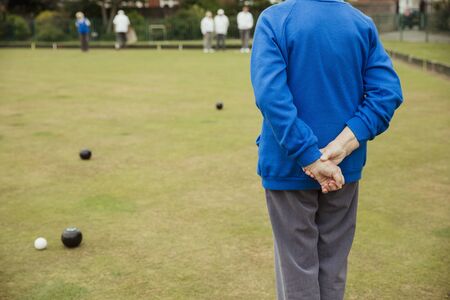 A rear view shot of an unrecognizable person spectating a lawn bowling game, standing with their hands behind their back.の写真素材