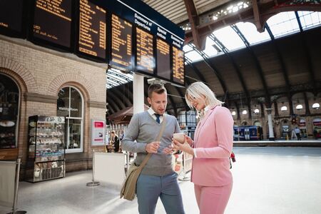 A businessman and businesswoman standing together at a train station. The woman is showing the man...