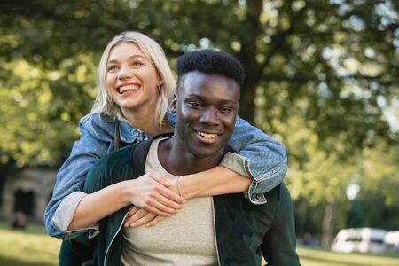 A close-up shot of a man giving a woman a piggyback lift through a park. They are both smiling.