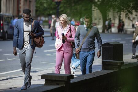A businesswoman is walking with two businessmen to work through the city.