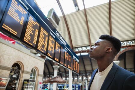 A businessman looking at a departure board in a train station.