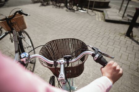Over the shoulder view of a woman riding a bicycle. The main focus is on the front of the bicycle and its basket.の写真素材