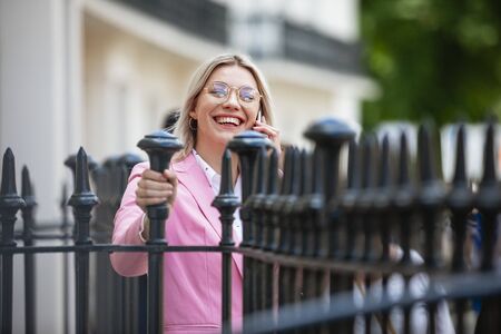 A businesswoman laughing while talking on her mobile phone. She is holding onto iron fencing.の写真素材