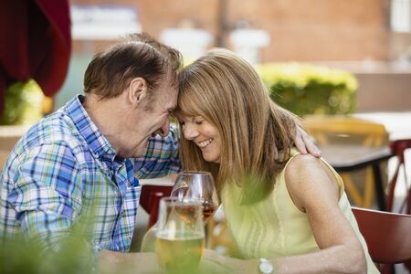A senior couple embracing each other while sitting at an outdoor bar having drinks.の写真素材