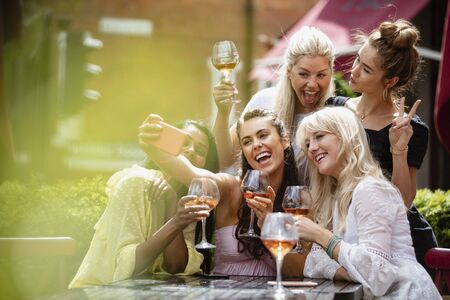 A group of female friends having drinks together outdoors at a bar while taking a selfie together.