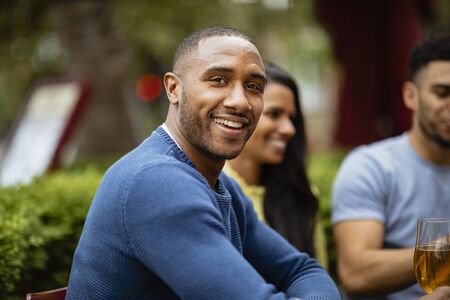 A group of friends having drinks outdoors at a bar. The main focus is a man smiling and looking at the camera.の写真素材