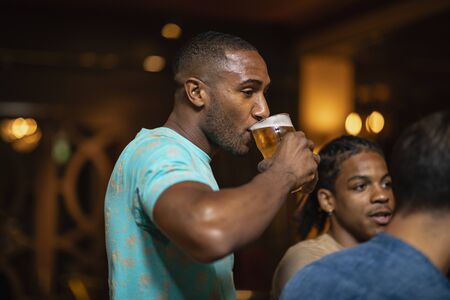 A group of male friends drinking together in a bar. The main focus is on a man drinking a pint of beer.の写真素材