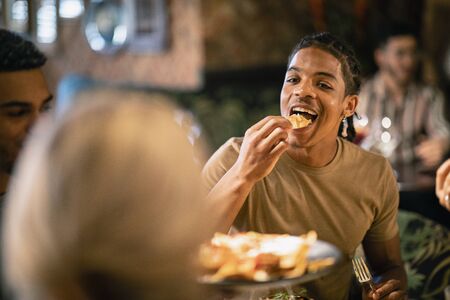A group of friends eating a meal at a restaurant. The main focus is on a mixed race man eating food.の写真素材