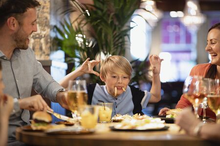 A family having a meal at a restaurant. A young boy is making them all laugh by making a face using food.の写真素材