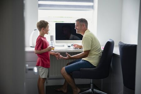 A side-view shot of a father and son sitting down using a computer, they are learning together.
