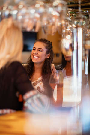 Female friends having drinks and laughing at a bar.の写真素材