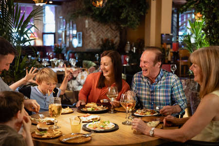 A family having a meal at a restaurant. A young boy is making them all laugh by making a face using food.の写真素材