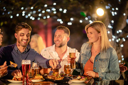 Group of friends drinking alcoholic drinks outdoors at a bar/restaurant, celebrating and having fun together.の写真素材