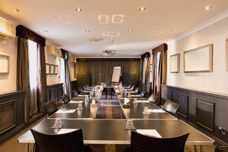 A shot of a large room with a table set up and ready for a business meeting with papers and glasses on each desk.の写真素材
