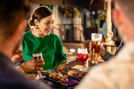 Friends drinking alcohol outdoors at a bar/restaurant, celebrating and having fun together.の写真素材