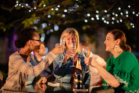 Group of diverse female friends drinking champagne outdoors at a bar/restaurant, celebrating and having fun together.の写真素材
