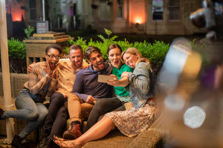 Group of diverse friends taking a selfie on a smart phone outdoors at a bar/restaurant, they are...
