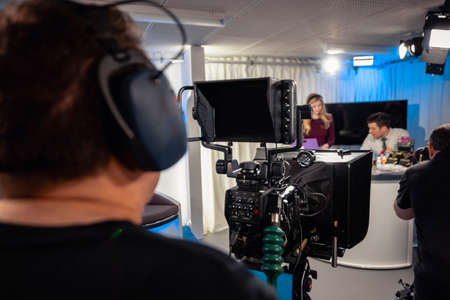 Over the shoulder view of a TV show in the process of being filmed in a studio. The presenters are...