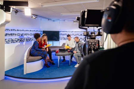 Over the shoulder view of a TV show in the process of being filmed in a studio. The presenters are...