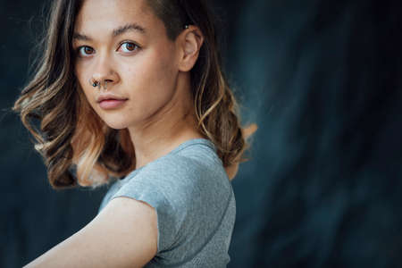 A young contented, trendy woman posing for the camera. She is standing in front of a backdrop.
