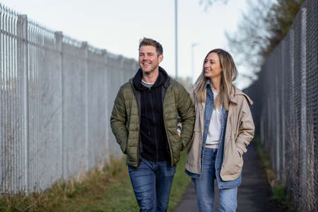 A front-view shot of a caucasian mid adult couple walking along a footpath together, they're smiling and enjoying eachother's company.の写真素材